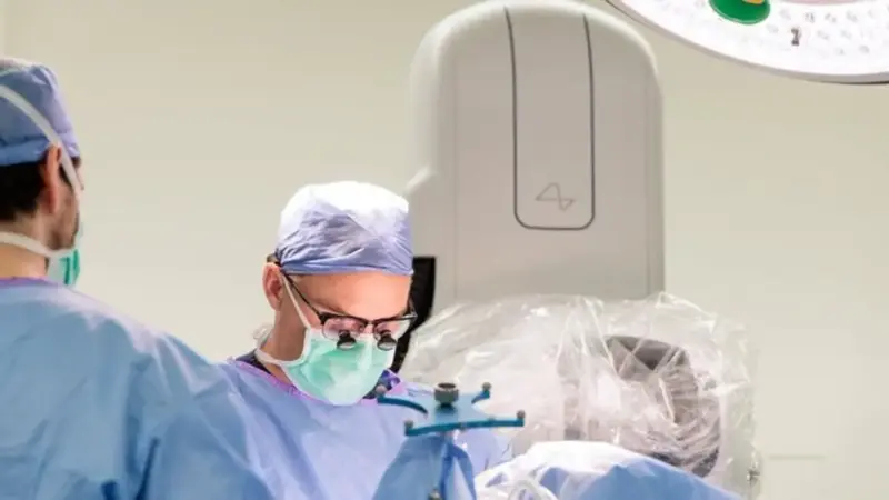 Ilustrasi prosedur bedah otomatis Neuralink menggunakan robot medis untuk menanamkan teknologi BCI ke otak manusia.